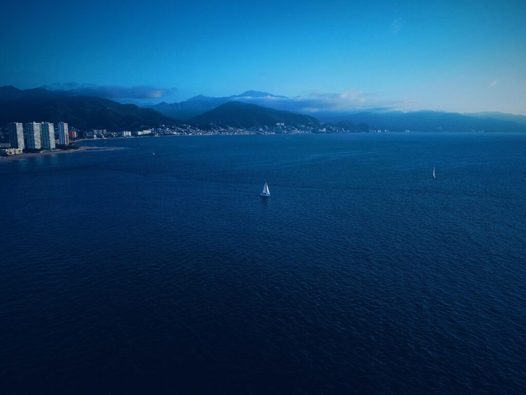 coast at dusk, a single sailboat in the middle of the ocean